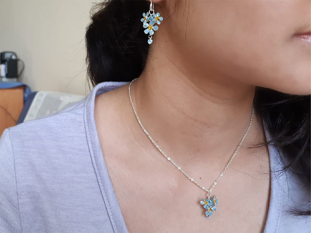 A minimalist, delicate sterling silver chain necklace with pendant and earrings. Pendant and earrings with cluster of tiny light blue Forget-Me-Not flowers with dangle crystal.