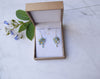 A minimalist, delicate sterling silver chain necklace with pendant and earrings. Pendant and earrings with cluster of tiny light blue Forget-Me-Not flowers with dangle crystal.