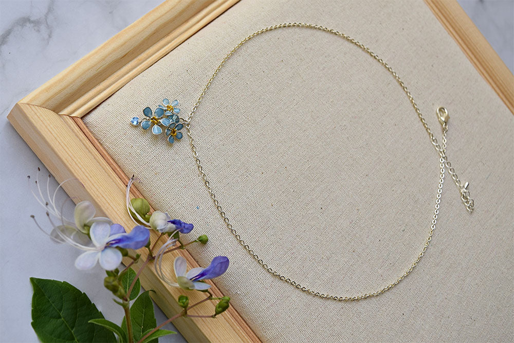 A minimalist, delicate sterling silver chain necklace with pendant and earrings. Pendant and earrings with cluster of tiny light blue Forget-Me-Not flowers with dangle crystal.